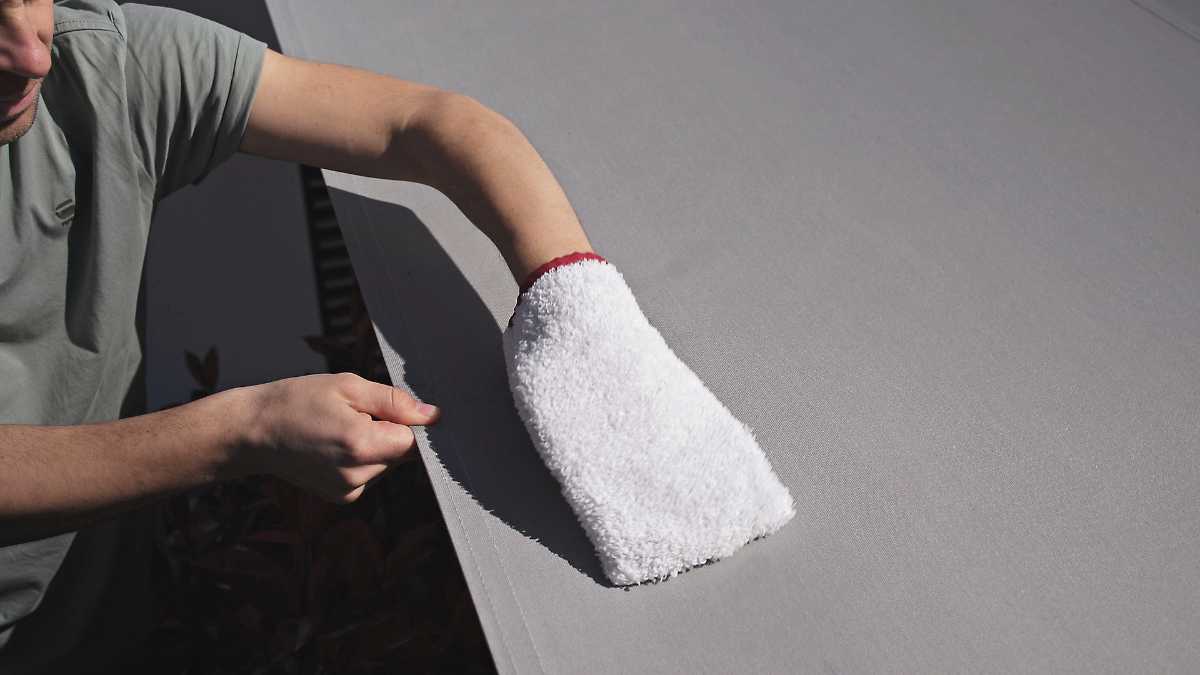 Person reinigt eine graue Oberfläche mit einem weißen Handschuh