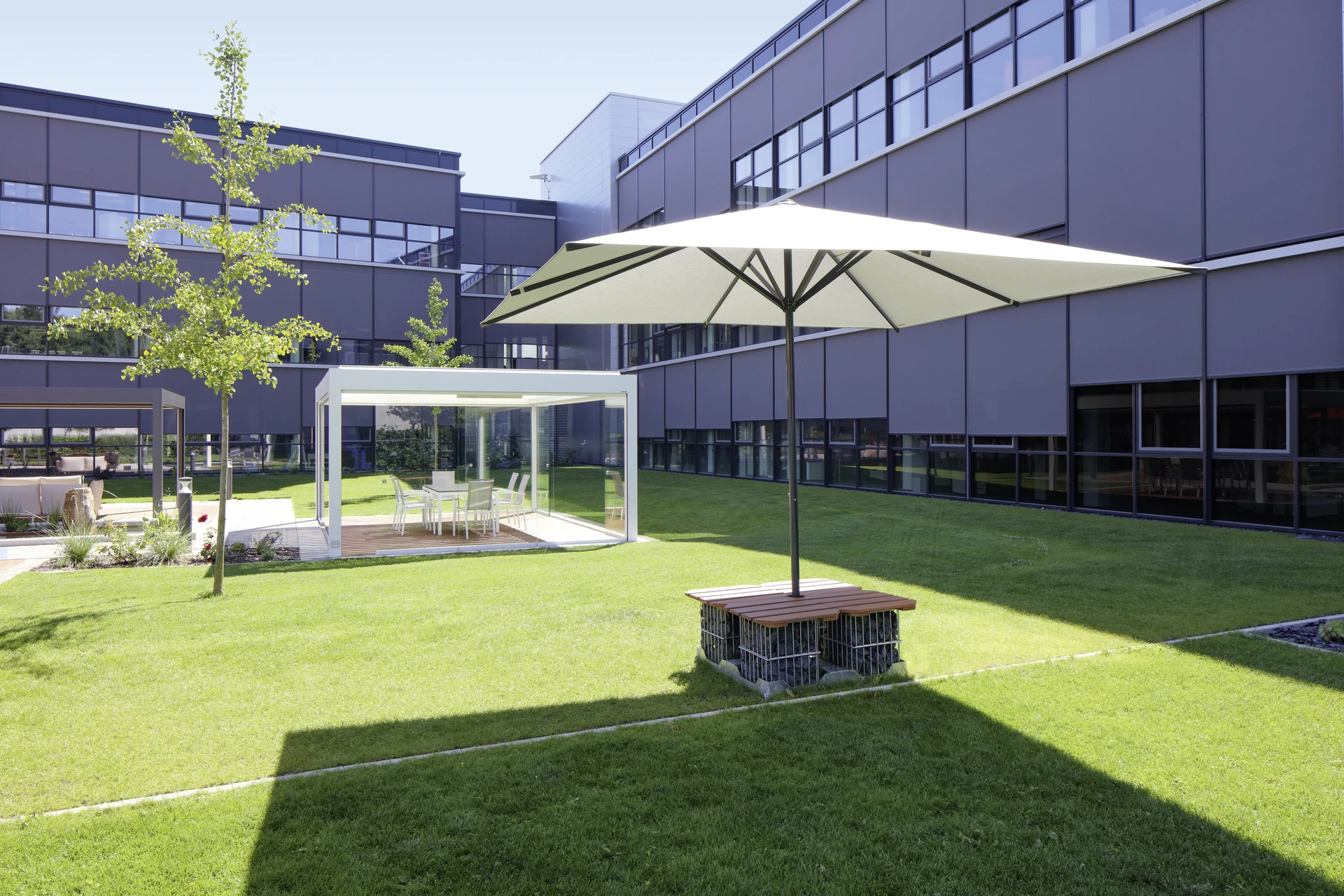 Moderne Außenansicht eines Bürogebäudes mit Sonnenschirm und Grünfläche