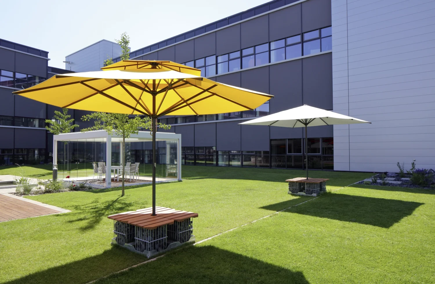 Moderne Firmengebäudefassade mit Sonnenschirmen auf grünem Rasen