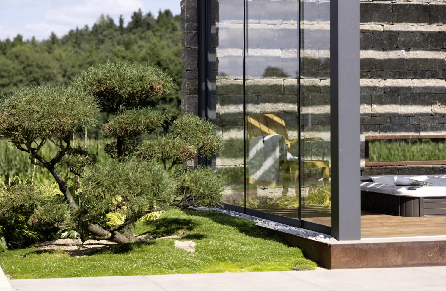 Moderner Garten mit Bonsai-Baum neben einem stilvollen Gebäude aus Glas und Stein